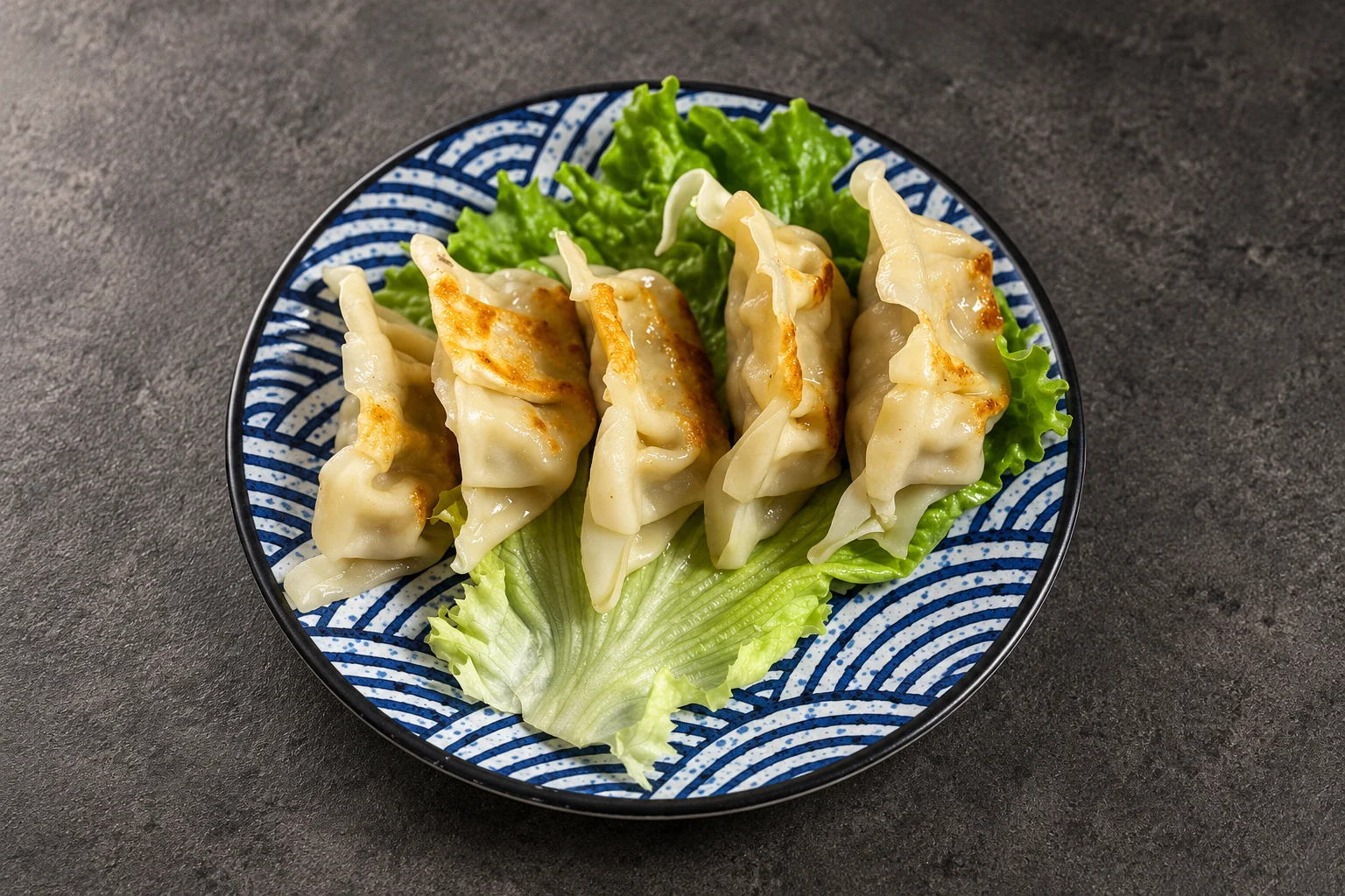 Gyoza on a lettuce leaf, plate with a blue wave pattern, dark concrete background.