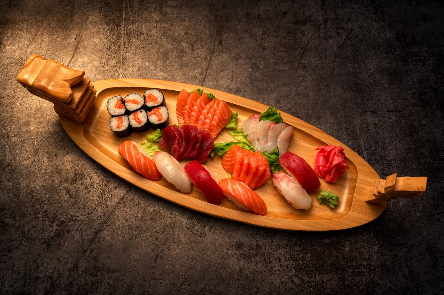 Sushi, maki and sashimi in a wooden boat-shaped tray, low light.