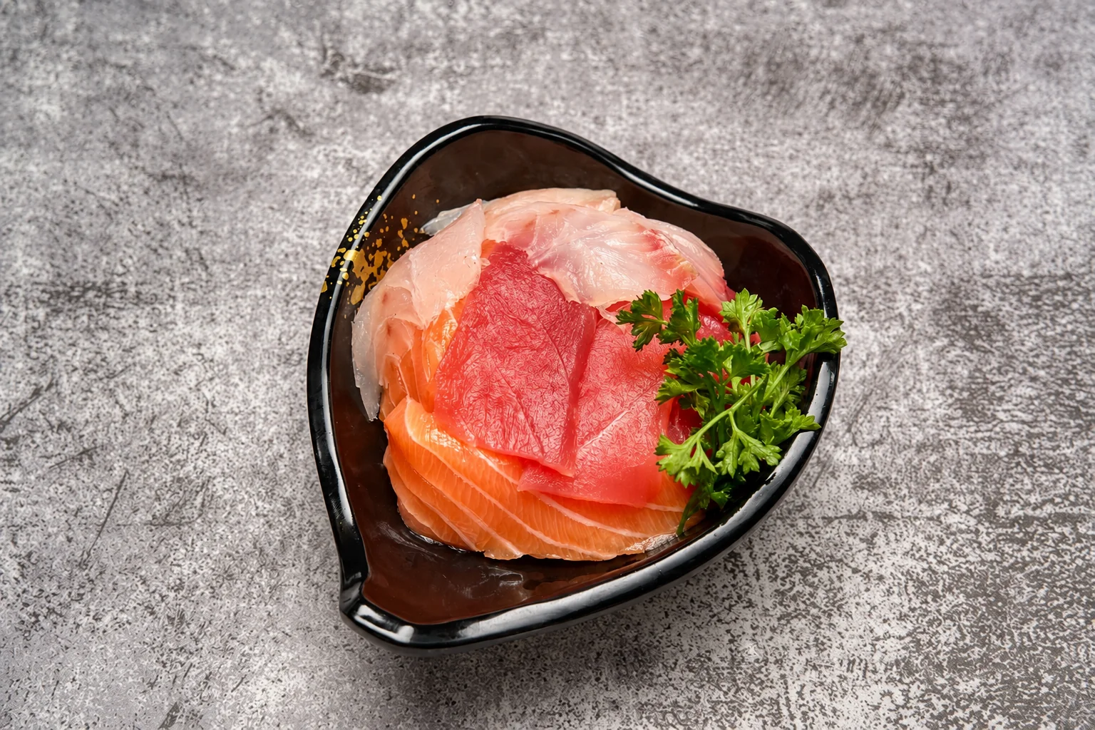Salmon and tuna sashimi with parsley in a black heart-shaped bowl, grey concrete background.
