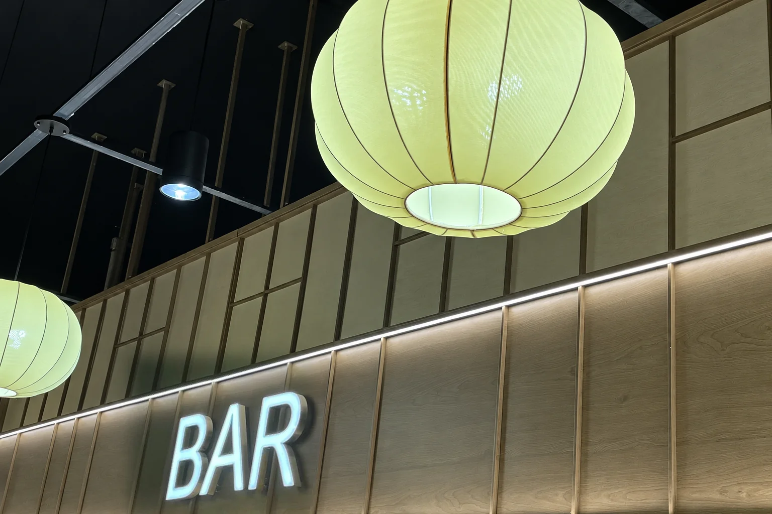 Light green paper lantern above a wooden wall with the lit BAR sign.
